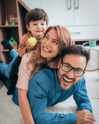 Imagem de uma família, o pai deitado e sobre ele a mãe e sobre a mãe o filhinho