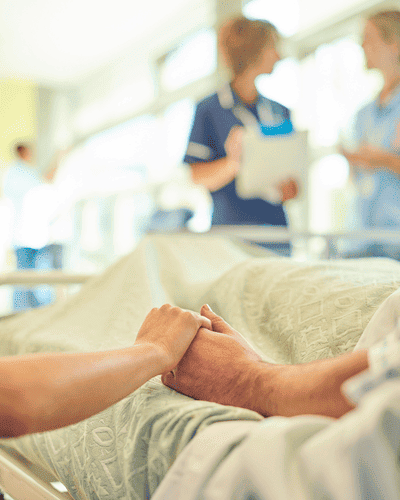 Imagem de duas enfermeiras e uma mão sob um braço no leito de hospital